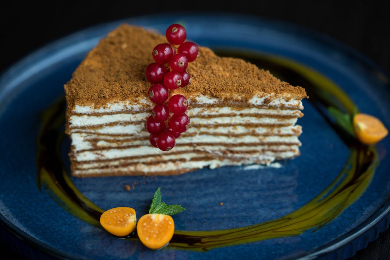 Delicious slice of layered honey cake topped with redcurrants, served elegantly on a blue plate.